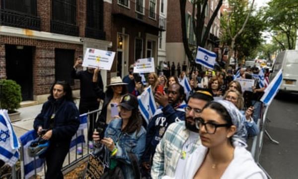 People hold Israeli flags within metal barriers on a street