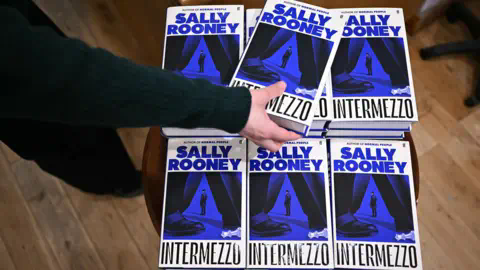 Getty Images A person's hand picks up a copy of Intermezzo - the new book by Sally Rooney - from a pile of books